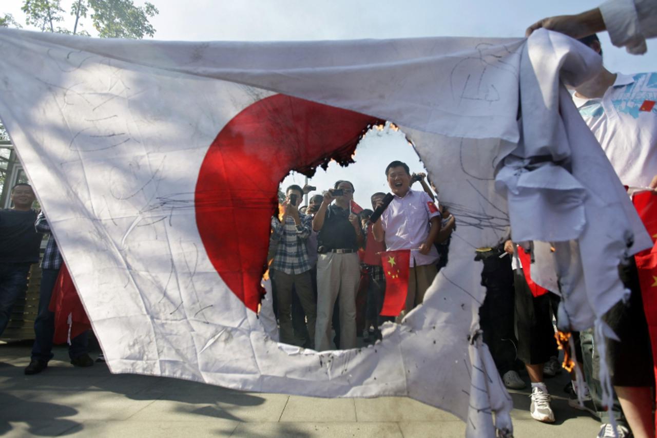 'Protesters laugh and take pictures next to a burned Japanese national flag during an anti-Japan protest in Wuhan, Hubei province September 16, 2012. Angry anti-Japan protesters took to the streets of