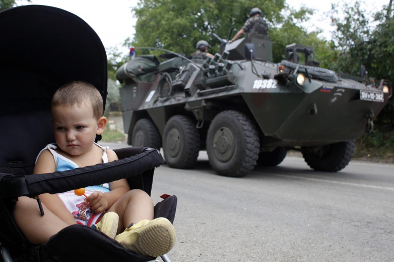 'A Kosovo Serb child sits in a pram as Slovenia\'s KFOR vehicle passes by in the village of Rudare near the town of Zvecan August 2, 2011. The NATO force in Kosovo said on Tuesday it had requested add