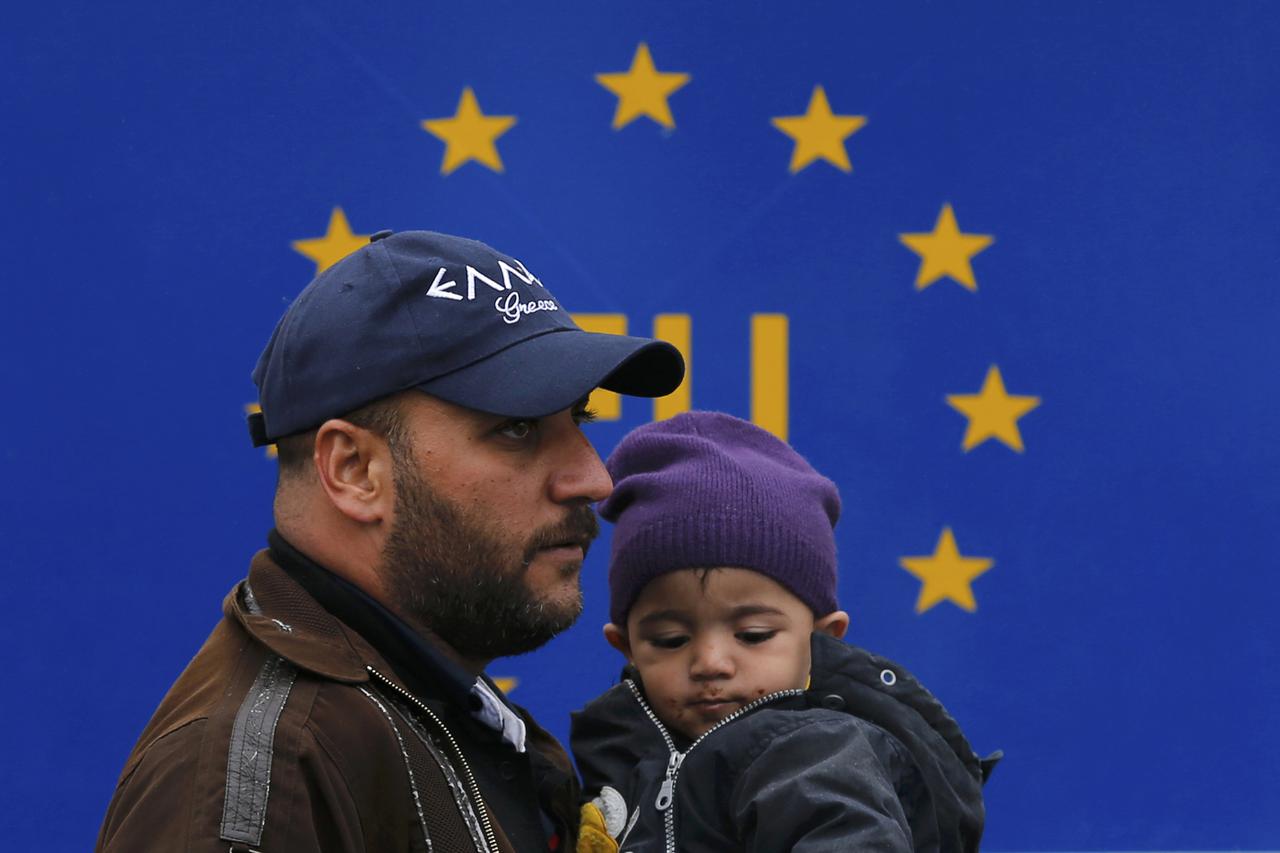 A migrant holds a child as he walks in front of an EU sign at the railway station in Tovarnik, Croatia September 29, 2015. REUTERS/Antonio Bronic
