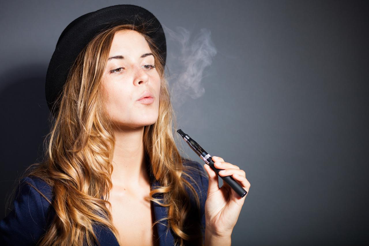 Elegant woman smoking e-cigarette with smoke, wearing suit and hat