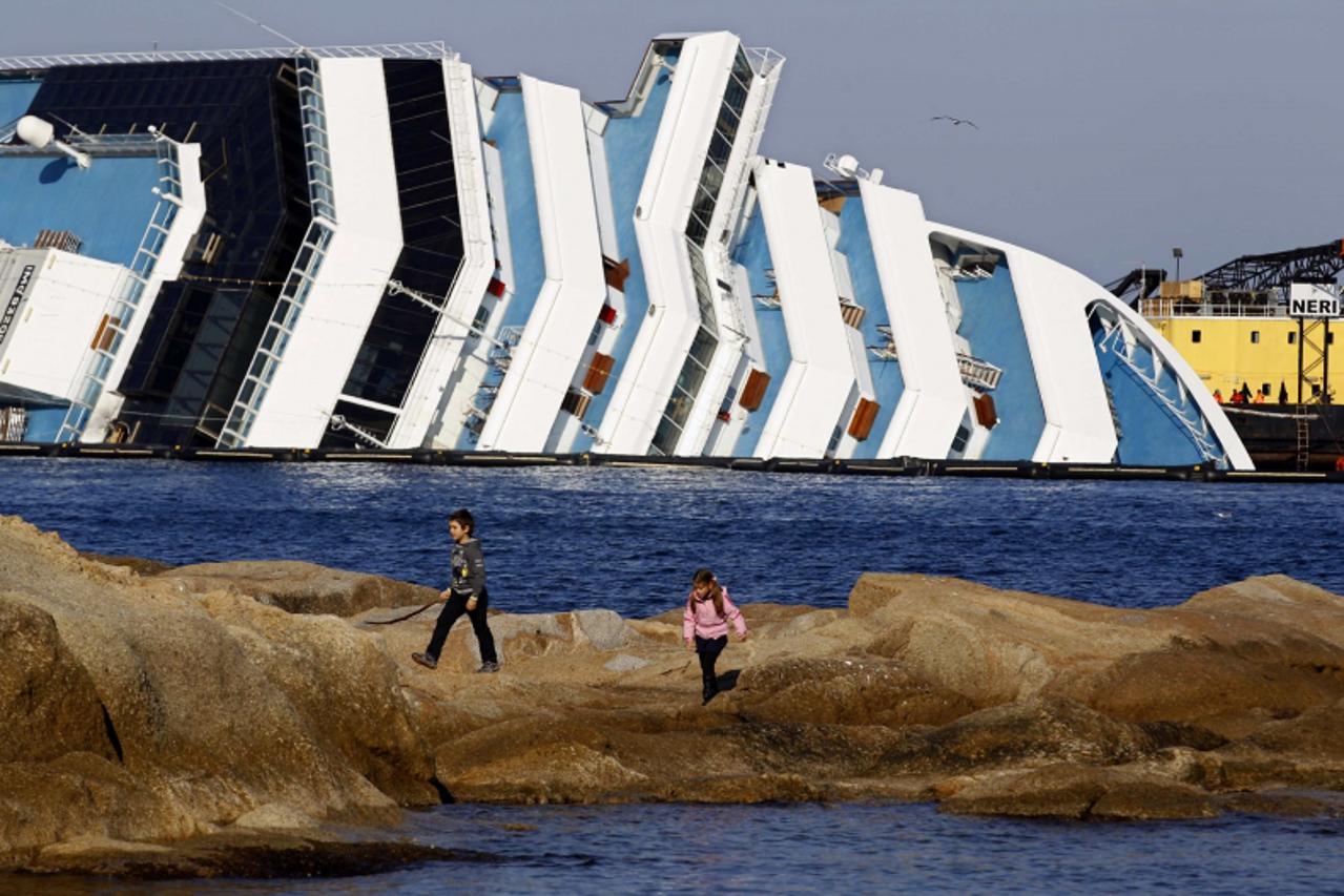 \'Children play in front of the Costa Concordia cruise ship, off the west coast of Italy, at Giglio island, February 5, 2012. Plans to remove the 2,300 tonnes of diesel fuel in the cruise ship\'s tank