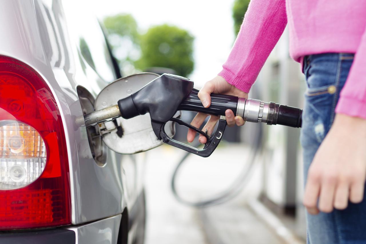Lady pumping gasoline fuel in car at gas station.