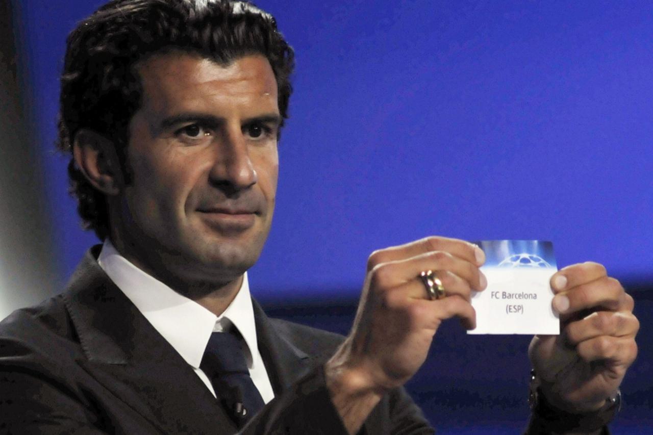 \'Former Portuguese soccer player Luis Figo holds up a card showing FC Barcelona during the Champions League draw at the Grimaldi Forum in Monaco August 25, 2011. Holders Barcelona have been drawn wit