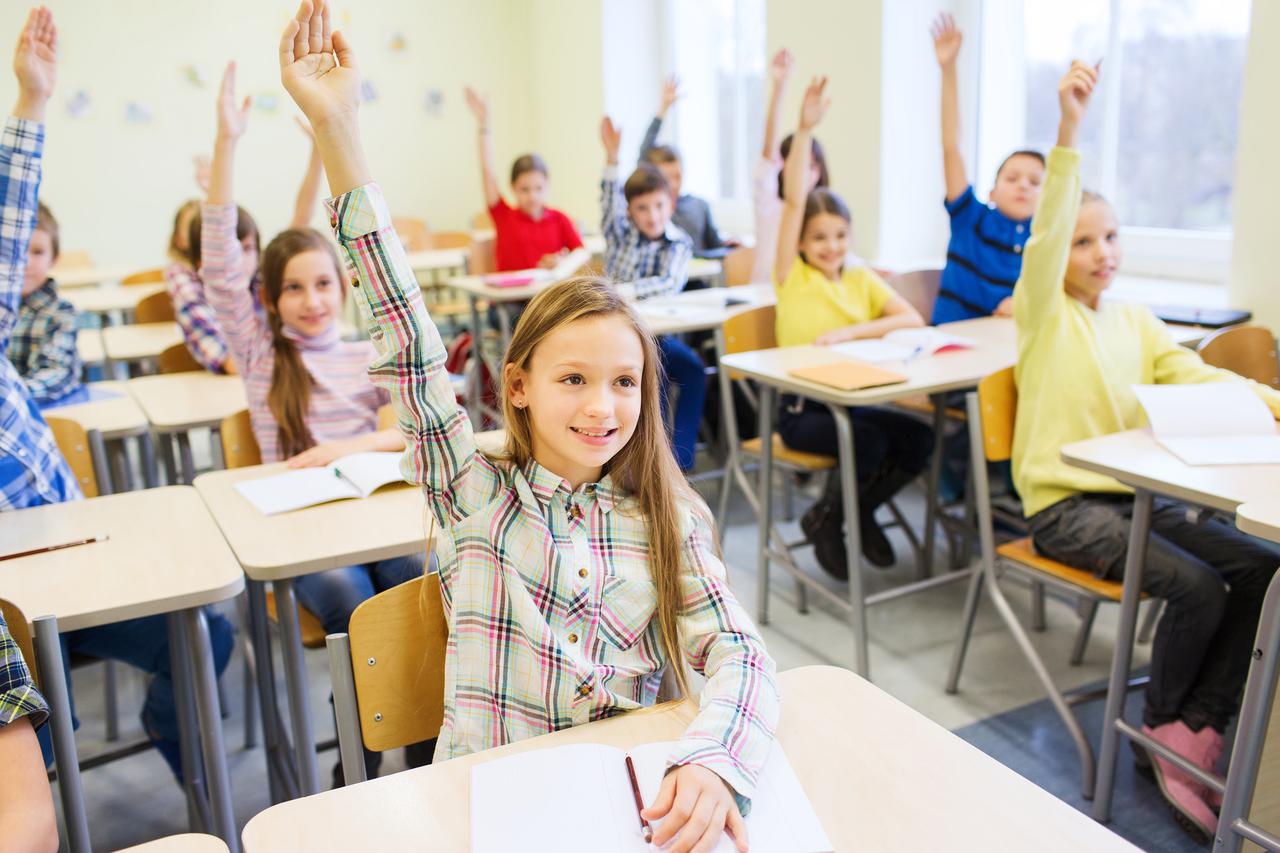 education, elementary school, learning and people concept - group of school kids with notebooks sitting in classroom and raising hands