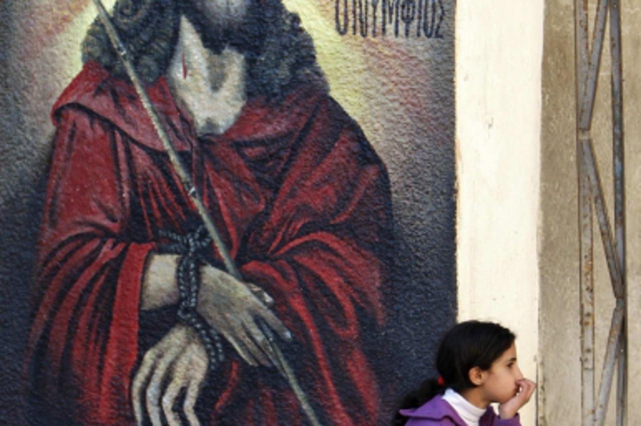 'A Palestinian Christian girl sits in front of a mural depicting Jesus in the West Bank village of Aboud near Ramallah, before Christmas December 16, 2010. REUTERS/Mohamad Torokman (WEST BANK - Tags: 