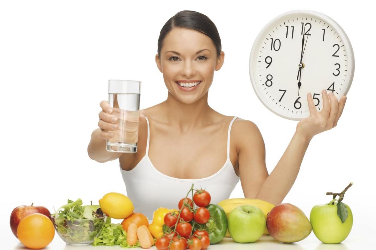 beautiful woman with healthy food water and clock