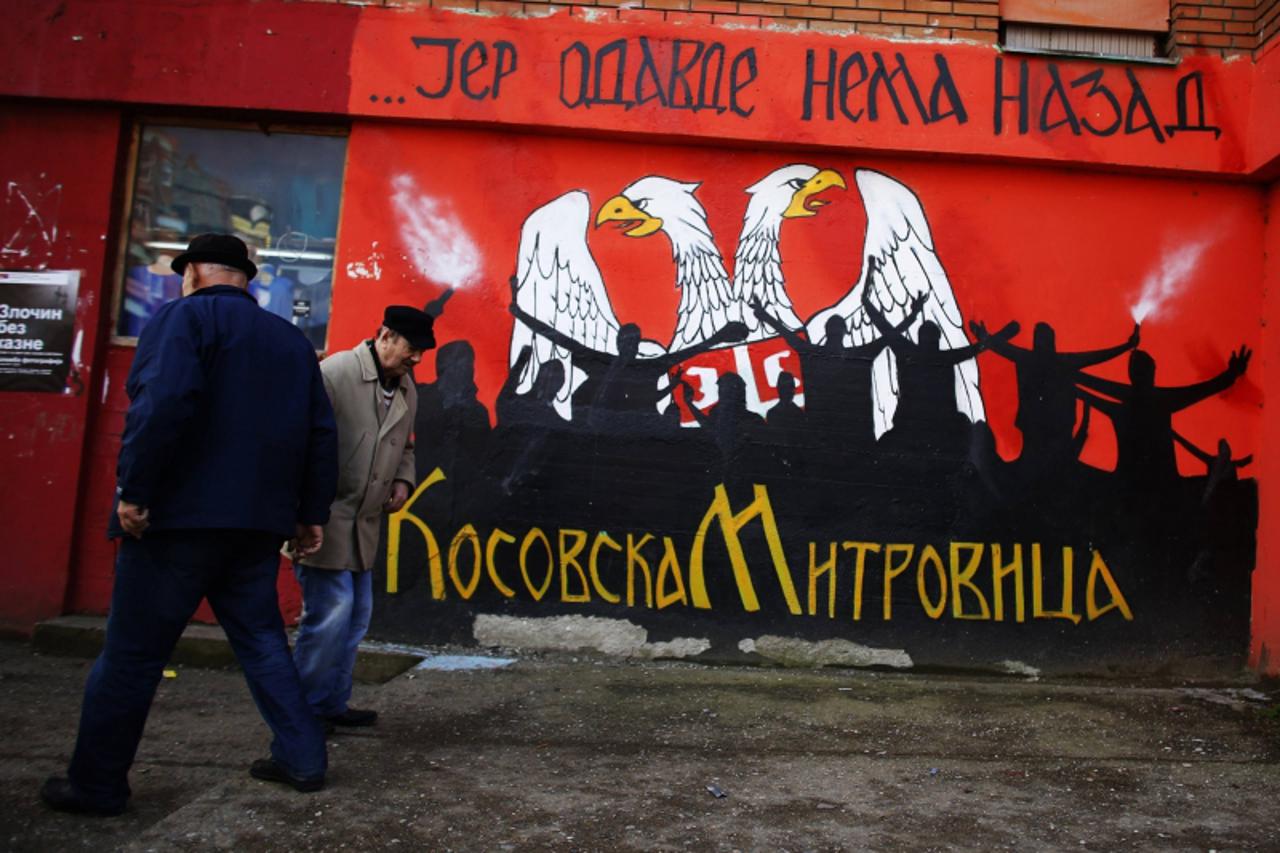 'Men walk past a graffiti reading: ''Because there is no turning back from here'', in the ethnically divided town of Mitrovica, March 19, 2013. Serbia does not recognise Kosovo's 2008 secession, 
