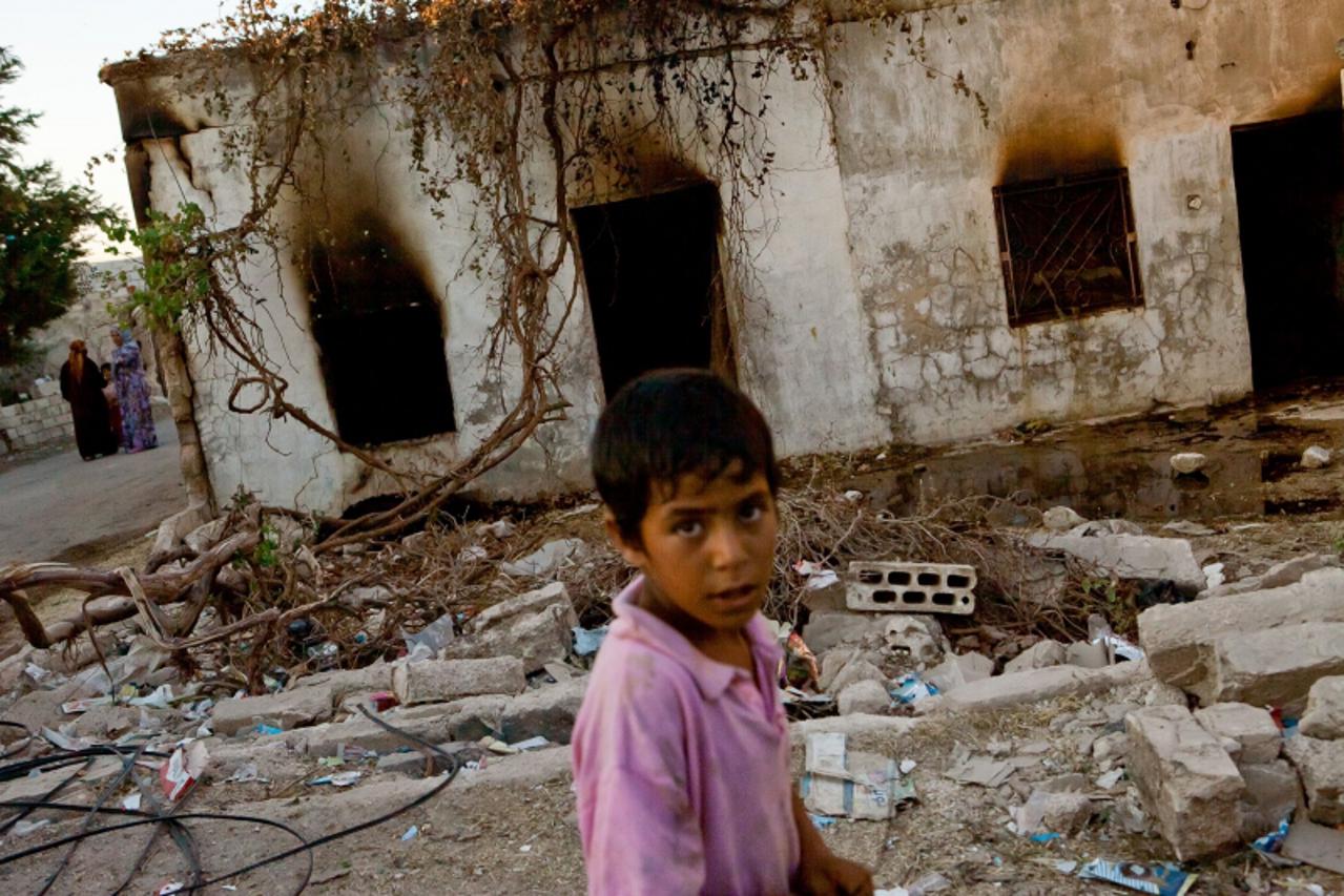 'A Syrian boy walks past a burnt house in the Syrian village of Treimsa, where more than 150 people were killed this week, in the central province of Hama on July 13, 2012. A variety of weapons were u